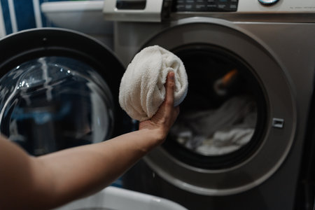 Housekeeper placing white towels into washing machine, preparing for laundry cycle in modern laundry...