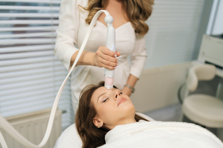 Vertical cropped shot of beautician doctor performing mesotherapy procedure on woman forehead, targeting skin rejuvenation and reducing wrinkles in cosmetology clinic. Concept of beauty treatment.の写真素材