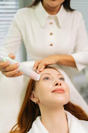 Beautician performing mesotherapy treatment using specialized tool on relaxed client face during professional skincare procedure in beauty salon. Concept of body and health care, alternative medicine.の写真素材