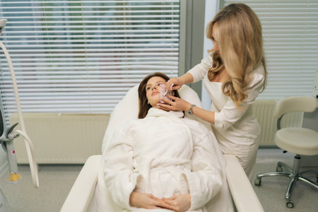 Front view of beautician applying markup grid on face of female patient, preparing for permanent makeup procedure in bright modern beauty salon. Concept of professional skincare, beauty treatment.の写真素材