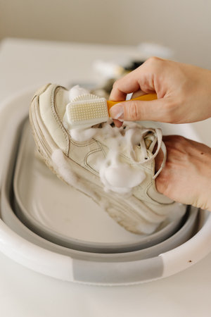 Vertical top view shot of cleaning white sneakers with small brush, removing mud stains from worn footwear in basin. Concept of hygiene, footwear free from dirt and bacteria for healthy lifestyle.の写真素材