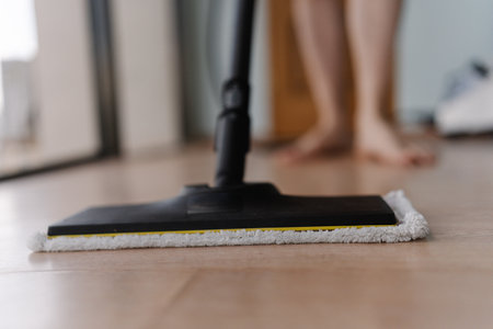Cropped shot of unrecognizable man washing hardwood floor with steam cleaner mop in modern apartment, ensuring hygiene and cleanliness, close-up. Concept of modern housekeeping appliance.の写真素材