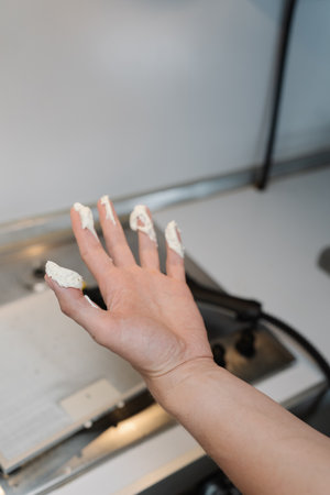 Vertical cropped shot of unrecognizable man holding moisturizing cream mixed with some white powder in hand, preparing skin treatment standing in kitchen setting, closeup. Concept of healthy lifestyleの写真素材