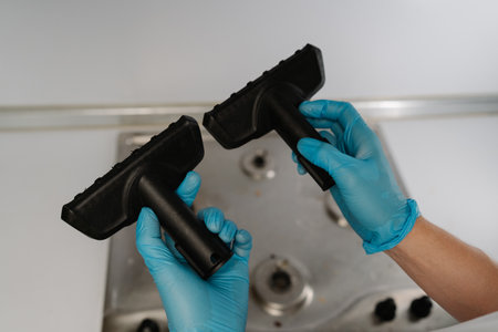 Close-up of unrecognizable man in gloves holding and comparing two different brushes for steam cleaning dirty stainless steel gas stove, evaluating options for effective appliance maintenance.の写真素材