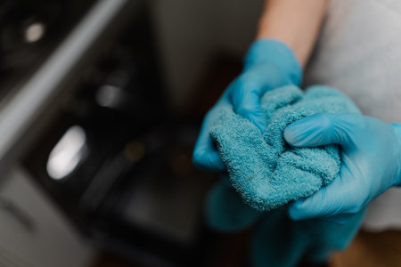 Cleaning service employee wearing gloves holding towel after cleaning modern kitchen oven, ensuring hygiene and cleanliness, close-up. Concept of domestic work, housekeeping and household.の写真素材
