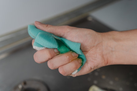 Housewife hand squeezing soapy water from sponge during cleaning dirty gas stove, to removing grime and grease, promoting hygiene and cleanliness in kitchen. Concept of domestic work and household.の写真素材