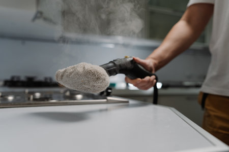 Cleaning service worker washing light kitchen countertop with sanitizing steam cleaner near stovetop, maintaining spotless domestic hygiene. Concept of maintenance modern home appliance.の写真素材