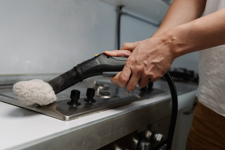Cleaning company worker using steam cleaner with cloth attachment sanitizing grimy gas stove surface, efficient kitchen cleaning and hygienic maintenance. Concept of easy housekeeping domestic life.の写真素材