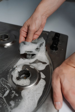 Close-up vertical shot of homeowner male tidying gas stove using detergent and rag during hygiene housekeeping in kitchen environments, closeup. Concept of domestic work, housework and household.の写真素材