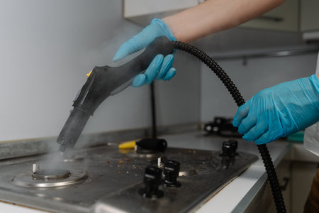 Male in gloves steam cleaning gas stove surface, eliminating burned food and grease, restoring kitchen surface to pristine condition with sanitizing process. Concept of modern housekeeping appliance.の写真素材