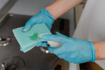 Housewife hand squeezing liquid detergent onto sponge, getting ready to cleaning kitchen gas stove, ensuring hygienic and spotless environment, close-up. Concept of housekeeping and household.の写真素材