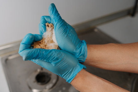 Close-up of hands in gloves squeezing heart-shaped sponge filled with soapy water, showing passion for cleaning and dedication to household tasks. Concept of domestic work, housekeeping and household.の写真素材