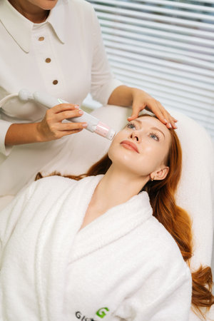 Vertical portrait of female client having mesotherapy treatment from professional beautician using specialized device, aiming to rejuvenate skin. Concept of rejuvenating skin, preventing aging.の写真素材