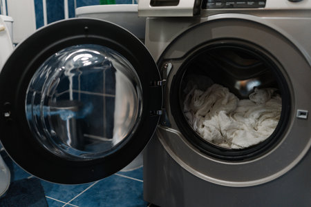 Modern washing machine featuring open door, showcasing drum filled with fluffy white towels, poised for wash cycle in modern bathroom environment, close-up, no people.の写真素材