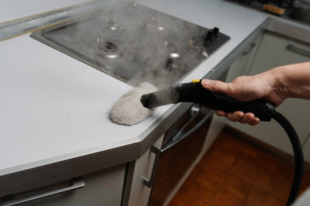 Close-up cropped shot of unrecognizable man brushing kitchen countertop with steam cleaner, promoting hygiene and disinfection in modern kitchen room, ensuring spotless and healthy space, closeup.の写真素材
