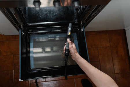 Top view of housewife male steam cleaning kitchen oven surface, targeting stubborn grease with cleaning equipment for spotless, sanitized cooking space. Concept of easy housekeeping domestic life.の写真素材
