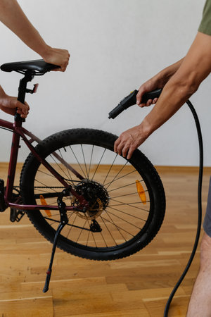 Closeup vertical cropped shot of two mechanics cleaning mountain bike wheel using steam cleaner, ensuring thorough maintenance and hygiene in professional workshop. Concept of bike service.の写真素材