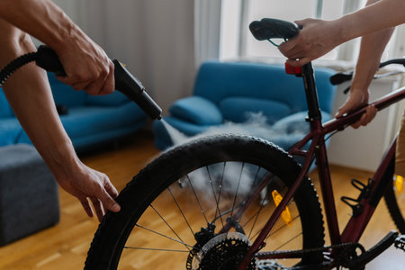 Two friends cyclists cleaning bicycle wheel using high-pressure steam cleaner, removing stubborn dirt at home, demonstrating meticulous bicycle maintenance technique, close-up. Concept of bike serviceの写真素材
