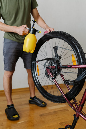 Cyclist washing mountain bike wheel with handheld water sprayer ensuring cleanliness and maintenance. Close-up of man washing bicycle wheel with spray bottle, removing dust and dirt from tire.の写真素材