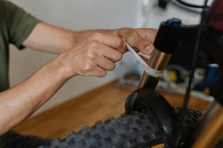 Bicycle mechanic male wiping bicycle front fork with clean white cloth, maintaining precision and mechanical integrity during maintenance process, close-up. Concept of bike maintenance and service.の写真素材