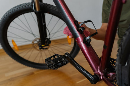 Bike mechanic cleaning and polishing mountain bike frame with cloth, emphasizing maintenance and repair skills in workshop environment, close-up. Concept of bike maintenance and service.の写真素材