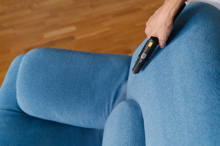 Professional cleaning service worker using steam cleaner to remove dirt and stains from blue sofa in home living room, ensuring hygiene and cleanliness. Concept of easy housekeeping domestic life.の写真素材