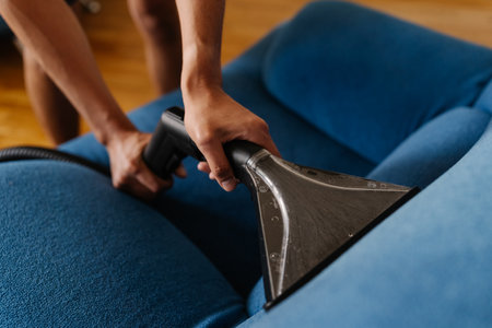 Cleaning service employee vacuuming blue upholstery, removing stubborn dirt and eliminating stains for spotless, sanitized furniture surface closeup. Concept of domestic work, housekeeping, household.の写真素材