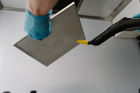 Shooting from below of cleaning service worker wearing gloves disinfecting kitchen extractor filter with steam cleaner, ensuring hygiene and cleanliness. Concept of modern housekeeping appliance.の写真素材