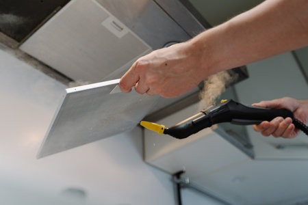 Close-up low-angle view of homeowner disinfecting kitchen extractor filter using steam cleaner in modern kitchen, ensuring hygiene and cleanliness. Concept of easy housekeeping domestic life, closeup.の写真素材