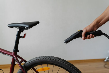 Cropped shot of unrecognizable man using steam cleaner to remove dirt and dust from tire of bicycle wheel at home, ensuring cleanliness, close-up. Concept of bike maintenance and service.の写真素材