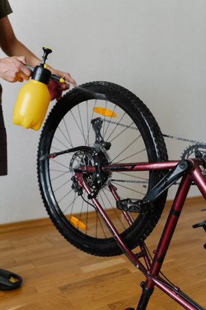Vertical shot of male washing mountain bike wheel with handheld water sprayer ensuring cleanliness and maintenance. Close-up of man cleaning bicycle wheel with spray bottle, removing dust from tireの写真素材