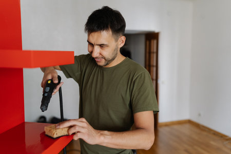 Portrait of bearded janitor male cleaning red shelf using steam cleaner and sponge, ensuring hygiene and spotless surface in commercial or residential setting. Concept of cleanliness and housekeeping.の写真素材
