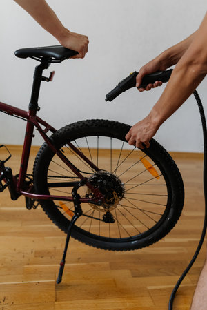 Vertical cropped shot of two mechanics cleaning mountain bike wheel using steam cleaner, ensuring thorough maintenance and hygiene in professional workshop. Concept of bike service.の写真素材