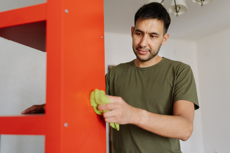 Portrait of cleaning company worker using cloth wiping dusty dirty red shelf showcasing commitment to cleanliness and hygiene, close-up. Concept of domestic work, housekeeping, household.の写真素材