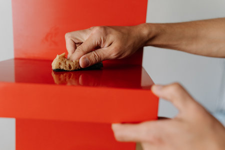 Close-up hand of housekeeper male cleaning red shelf surface using sponge and detergent ensuring spotless and hygiene at home. Concept of domestic work, housekeeping and household.の写真素材
