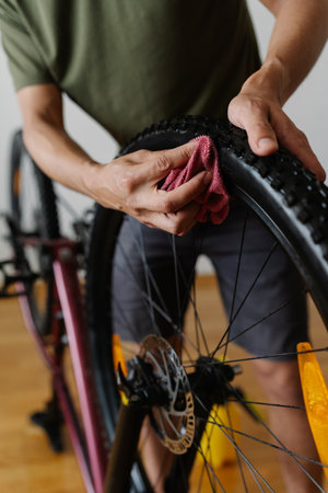 Close-up vertical shot of bike owner cleaning dirty tire of bicycle with cloth, focusing on detail to maintain optimal performance at home. Concept of bike maintenance and service.の写真素材