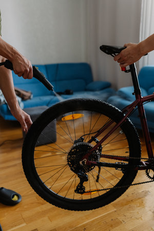 Two people cleaning bicycle wheel with steam cleaner, removing dirt and grime in cozy home environment, ensuring thorough maintenance and hygiene at domestics interior. Concept of bike service.の写真素材