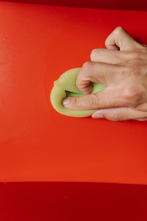 Vertical cropped shot of man using cleaning rag, wiping dusty dirty red shelf with shiny surface, showcasing commitment to cleanliness and hygiene. Concept of domestic work, housekeeping, household.の写真素材
