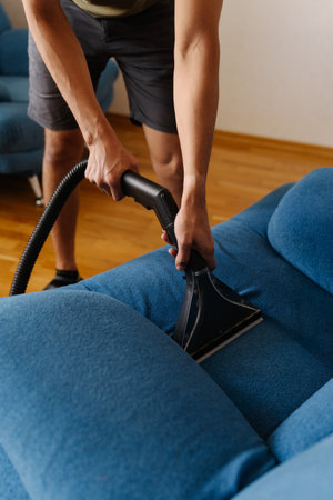 Housekeeper employee vacuuming blue upholstery, removing stubborn dirt and eliminating stains for spotless, sanitized furniture surface closeup. Concept of domestic work, housekeeping, household.の写真素材