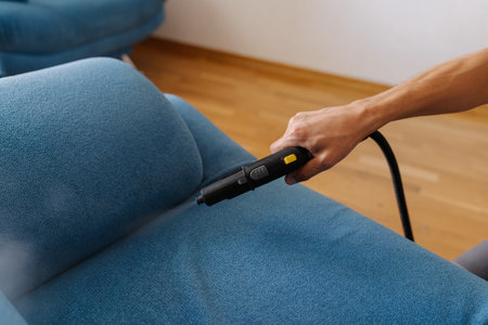 Close-up of cleaning service worker using steam cleaner machine and cleaning blue sofa, removing mites with hot steam in living room. Concept of hygiene and cleanliness in domestic environment.の写真素材