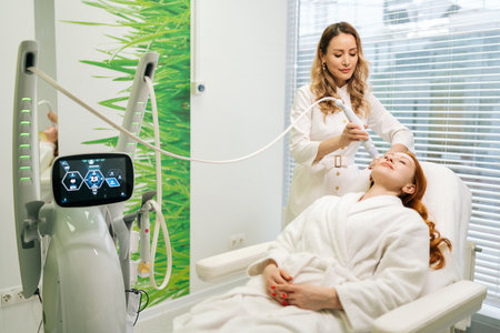 Beautician performing mesotherapy treatment on female face client using specialized device, promoting skin rejuvenation through microinjections in cosmetology clinic. Concept of beauty treatment.の写真素材
