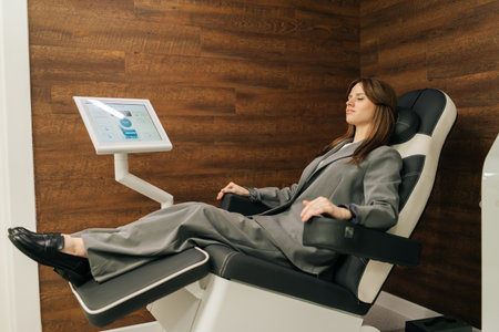Side view of sick businesswoman in suit sitting on ergonomic chair for pelvic floor muscle examination in modern clinic, looking away. Concept of innovative healthcare technology.の写真素材