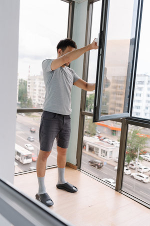 Vertical shot of housewife male cleaning large residential window using squeegee and spray bottle,...
