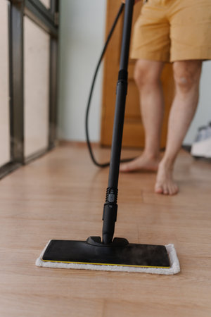 Vertical cropped shot of wooden floor receiving deep cleaning through powerful steam mop, generating hot steamy vapor and showcasing thorough household sanitation method, close-up.の写真素材