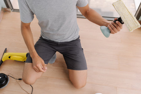 Professional cleaner male organizing cordless window cleaning tools, spray bottle, cleaning pad, alongside robotic vacuum and charging station, preparing for efficient workspace maintenance, close-up.の写真素材