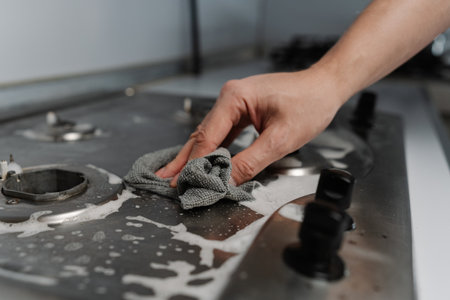 Close-up cropped shot of unrecognizable man using rag and detergent cleaning stainless steel gas...