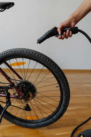 Vertical cropped shot of cyclist male using steam cleaner to remove dirt and grime from tire of bicycle wheel at home, ensuring cleanliness, close-up. Concept of bike maintenance and service.の写真素材