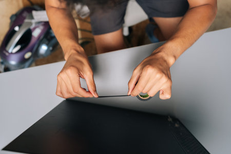 High-angle view of technician applying piece of black electrical tape to edge of computer case,...
