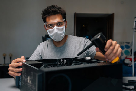 Portrait of technician in face mask and safety glasses looking at camera cleaning computer case...