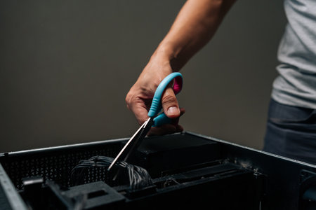 Close-up of technician hand using scissors to cut cable inside desktop computer, performing...
